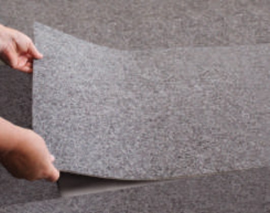 Hands lifting the edge of a grey gym floor cover tile